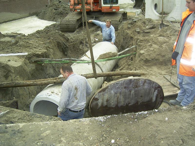 05-10-2004 de grondwerkers zijn bezig om de kabels vrij te maken zodat de rioolbuis er onderdoor kan en aangesloten op het bestaande riool. en de kraanmichinist trekt de kabels omhoog.