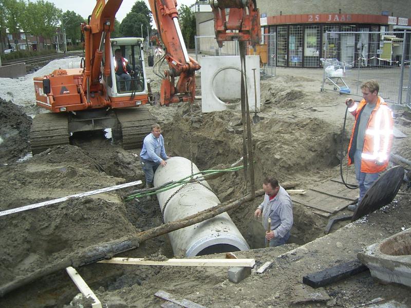 05-10-2004 de grondwerkers zijn bezig om de kabels vrij te maken zodat de rioolbuis er onderdoor kan en aangesloten op het bestaande riool. en de kraanmachinist trekt de kabels omhoog.