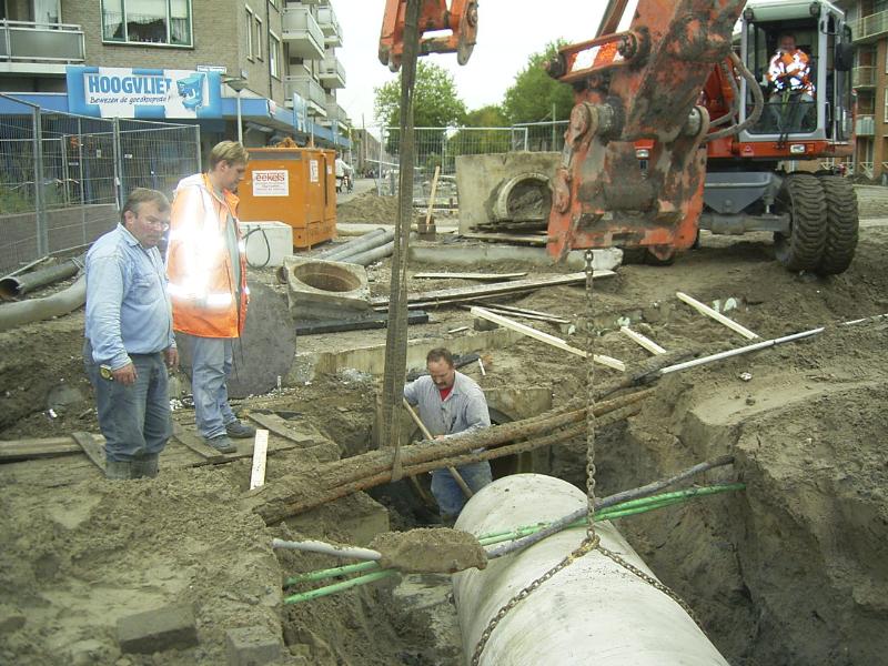 05-10-2004 de grondwerkers zijn bezig om de kabels vrij te maken zodat de rioolbuis er onderdoor kan en aangesloten op het bestaande riool. en de kraanmichinist trekt de kabels omhoog.